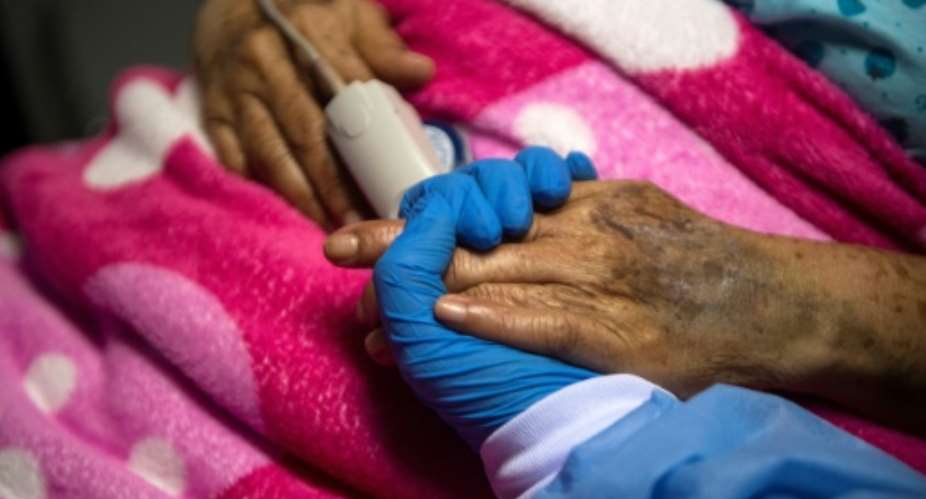A health worker holds the hand of a Covid patient in Peru. Health experts say that taming the pandemic over the next year is possible.  By ERNESTO BENAVIDES AFPFile