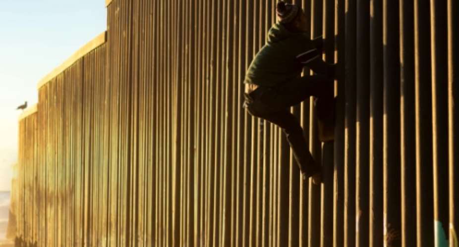 A Honduran migrant climbs the US-Mexico border fence on December 8, 2018.  By Guillermo Arias AFP