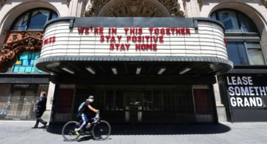 A Los Angeles cyclist in a face mask rides past the Million Dollar Theater, closed due to the coronavirus pandemic, with words on the marqee calling for togetherness.  By Frederic J. BROWN AFP