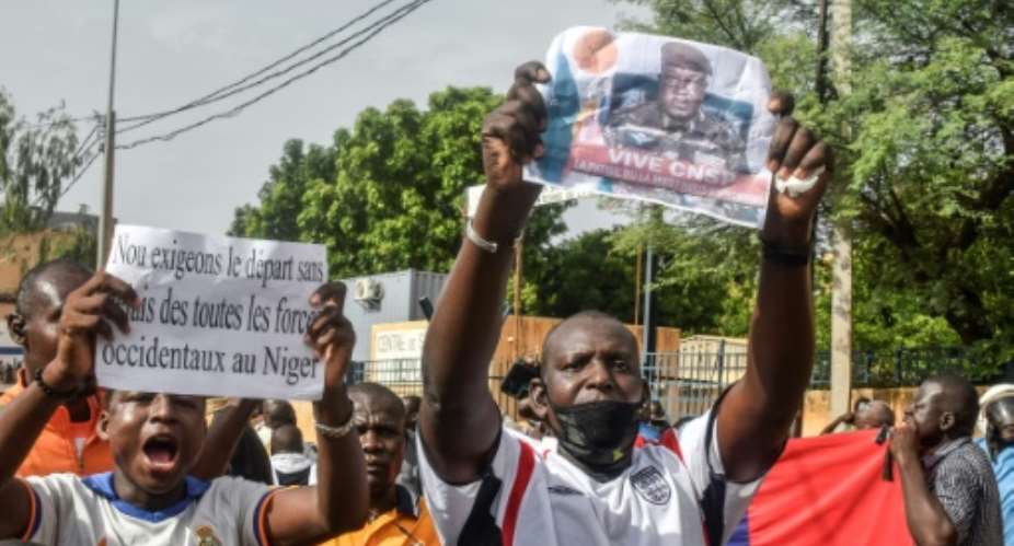 A man at a demonstration in Niamey in Sunday holds up a sign reading 'We demand the departure of all western forces from Niger' while another holds up a picture of coup leader General Abdourahamane Tiani.  By - AFP