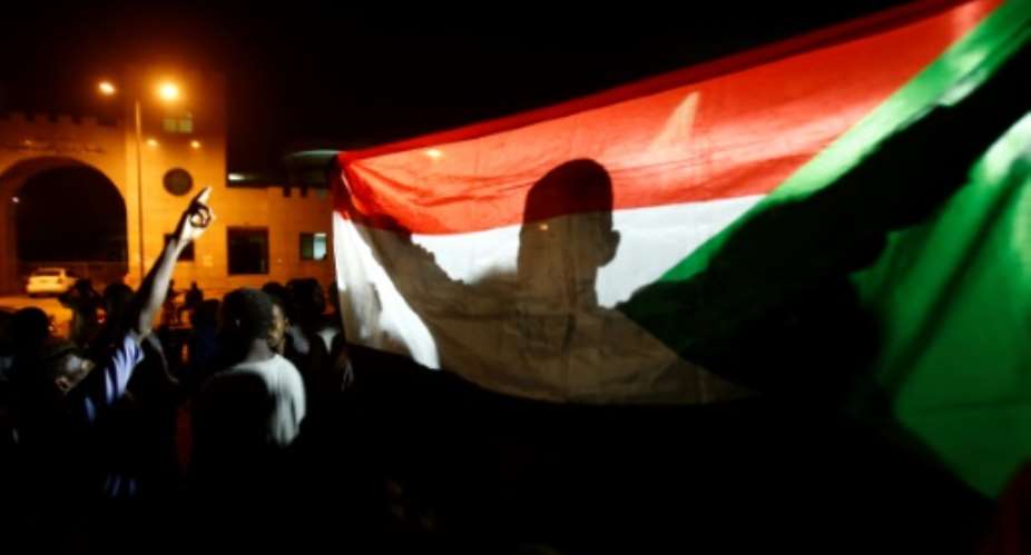 A man holds the Sudanese flag during a night-time demonstration outside the army headquarters in Khartoum on May 30, 2019.  By ASHRAF SHAZLY AFPFile