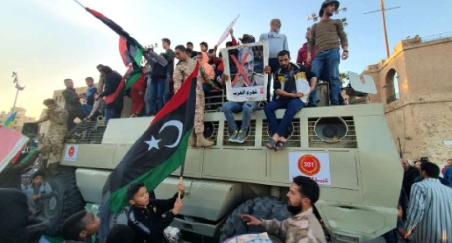 A man holds up a sign showing the face of Libyan strongman Khalifa Haftar crossed out with a red X, as he sits with others on an armoured military vehicle of forces loyal to the UN-recognised Tripoli-based Government of National Accord.  By Mahmud TURKIA AFPFile