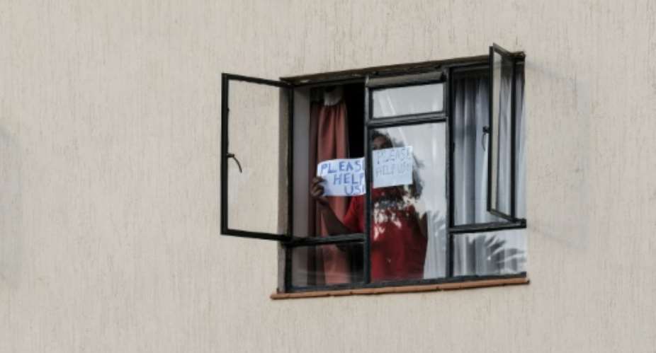 A man in mandatory quarantine in Kenya holds a sign reading help me out of the window of a facility in Nairobi.  By - AFP