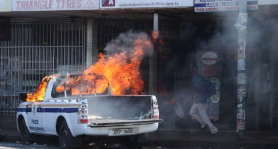 A man runs past Zimbabwean police car allegedly set ablaze by supporters of the opposition party Movement for Democratic Change Tsvangirai faction MDC-T during a march against police brutality in Harare on August 24, 2016.  By Wilfred Kajese AFPFile