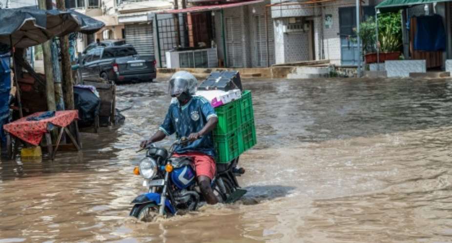 A man steers his motorcycle through Dakars flooded streets on October 5, 2026.  By SEYLLOU (AFP)
