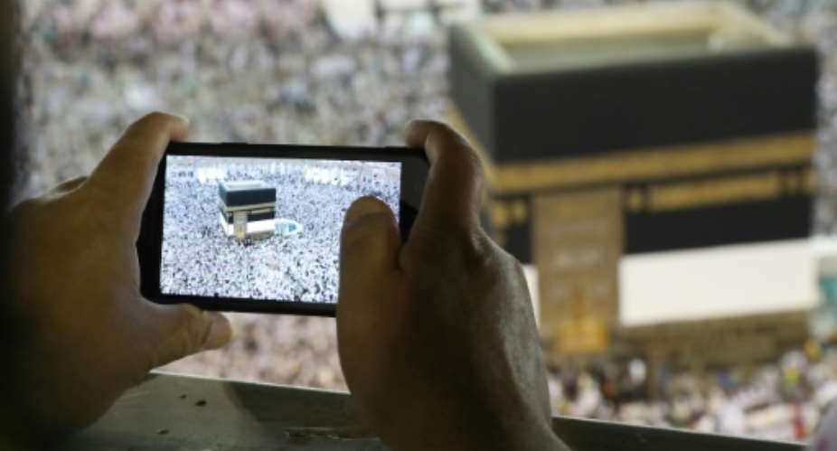 A man takes a picture of Muslim worshippers performing prayers around the Kaaba, Islam's holiest shrine, at the Grand Mosque in Saudi Arabia's holy city of Mecca on August 15, 2018.  By Bandar Al-DANDANI AFP