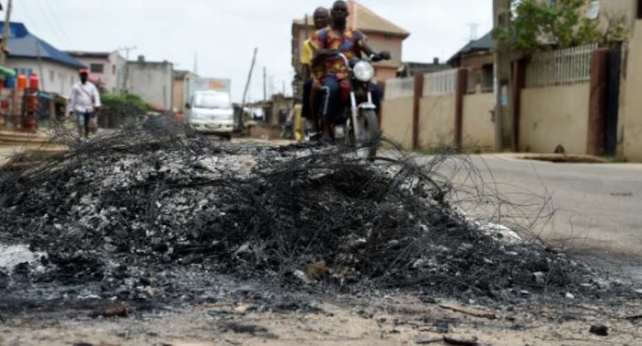 A motorcycle taxi in the district of Ojodu drives past the remains of a fire set to ward off gangs of robbers.  By PIUS UTOMI EKPEI AFP