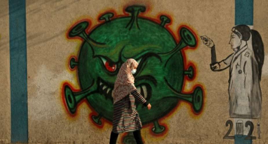 A Palestinian woman, wearing a protective mask amid the COVID-19 pandemic, walks past a coronavirus-inspired mural in Gaza City.  By Mohammed ABED AFPFile