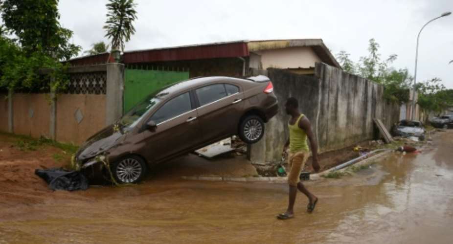 A pedestrian walks past  a vehicle on a flood-hit street in Abidjan.  By Sia KAMBOU AFPFile