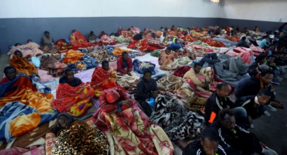 A picture taken on December 11, 2017 shows African migrants sitting in the Tariq Al-Matar migrant detention centre on the outskirts of the Libyan capital Tripoli.  By Mahmud TURKIA AFP