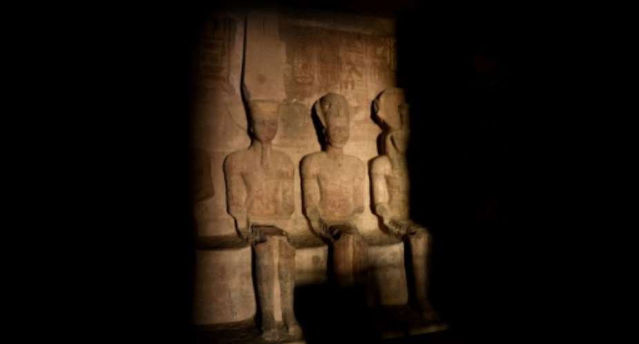 A picture taken on October 22, 2016, shows a ray of light illuminating the statue of Ramses II inside the temple of Abu Simbel in Egypt.  By MOHAMED EL-SHAHED AFP