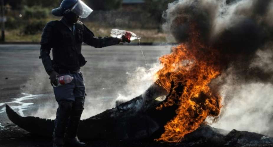 A policeman tries to extinguish a fire after demonstrators burnt tyres to barricade a road during violent protests in Ennerdale.  By MUJAHID SAFODIEN AFPFile