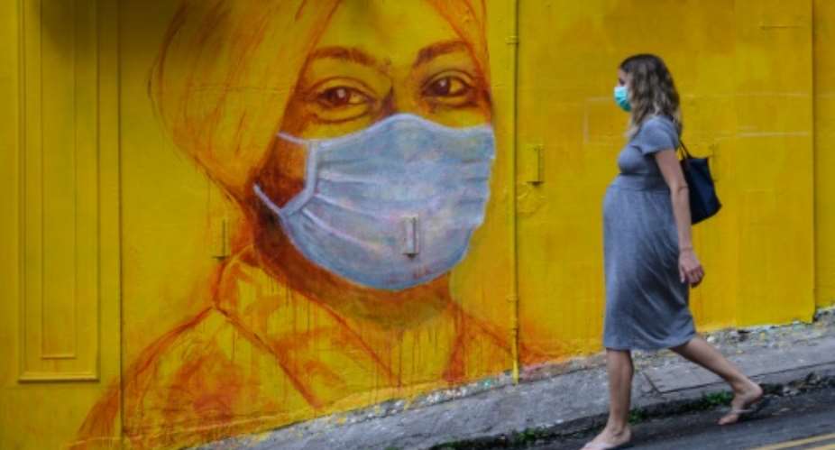 A pregnant woman wearing a face mask as a precautionary measure walks past a street mural in Hong Kong.  By ANTHONY WALLACE AFP
