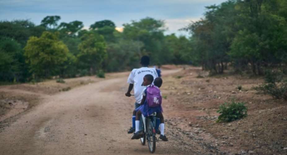 A relative pedals two students to school safely on a donated bicycle near Zimbabwe's Hwange National Park.  By Zinyange Auntony AFP