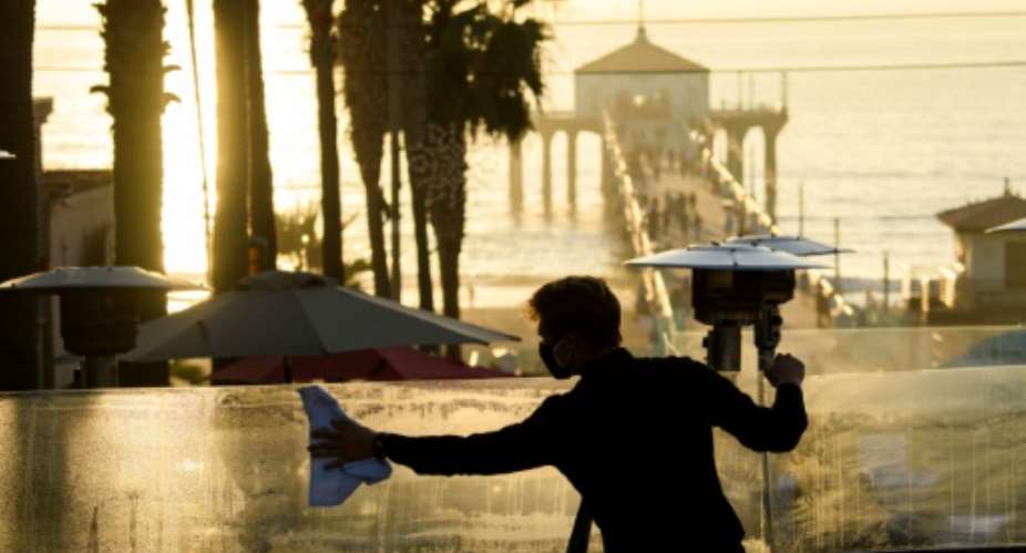 A restaurant employee cleans a plexiglass table divider while preparing for outdoor dining service in Manhattan Beach, California, a few hours before the start of the new 10:00 pm to 5:00 am curfew.  By Patrick T. Fallon AFP