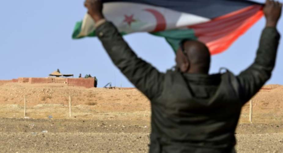 A Saharawi man holds up a Polisario Front flag in the Al-Mahbes area near Moroccan soldiers guarding the wall separating the Polisario controlled Western Sahara from Morocco on February 3, 2017.  By STRINGER AFP