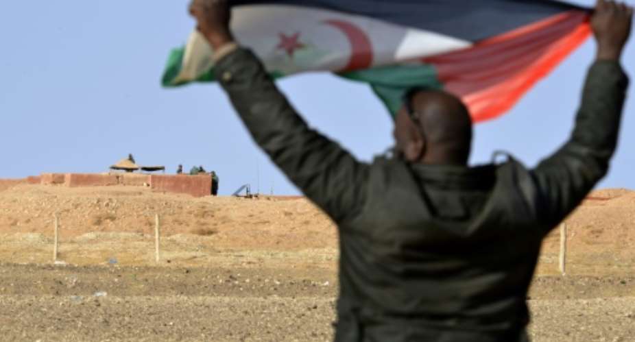 A Sahrawi man holds up a Polisario Front flag in the Al-Mahbes area near Moroccan soldiers guarding a wall separating Polisario-controlled parts of Western Sahara from Morocco on February 3, 2017.  By STRINGER AFP