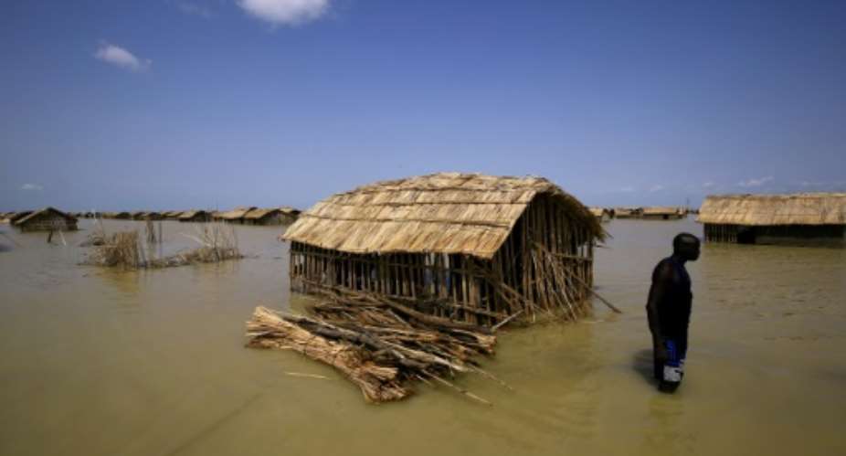 A South Sudanese refugee tries to repair his hut in flooded waters from the White Nile at a refugee camp which was inundated after heavy rain near in al-Qanaa, on September 14, 2021.  By ASHRAF SHAZLY (AFP/File)