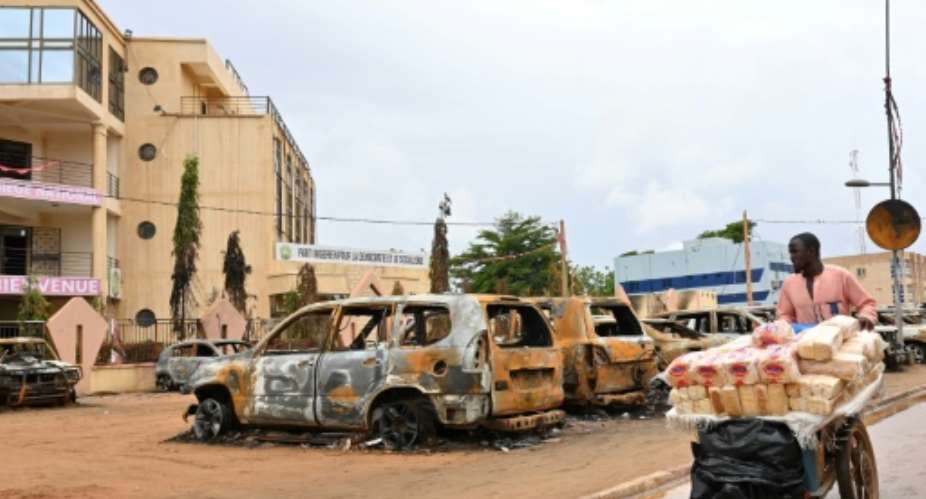 A street vendor pushes his cart past burnt-out cars outside Bazoum's party HQ in Niamey.  By - AFP