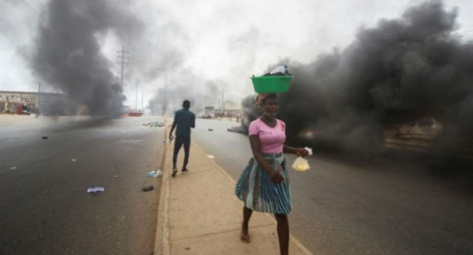 A street vendor walks past smoke from burning tyres during a anti-government demonstration in Luanda on October 24, 2020.  By Osvaldo Silva AFP