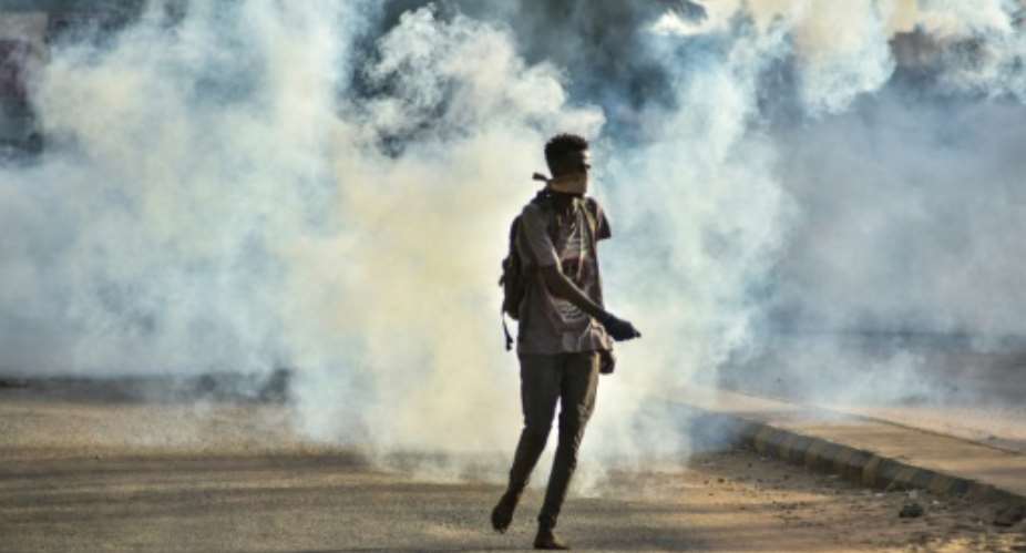 A Sudanese protester walks as tear gas fired by security forces swirls around on October 27.  By - AFP