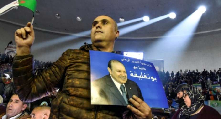 A supporter of Algeria's National Liberation Front holds up a poster of President Abdelaziz Bouteflika during a pre-campaign party rally in Algiers on February 9, 2019.  By RYAD KRAMDI AFP