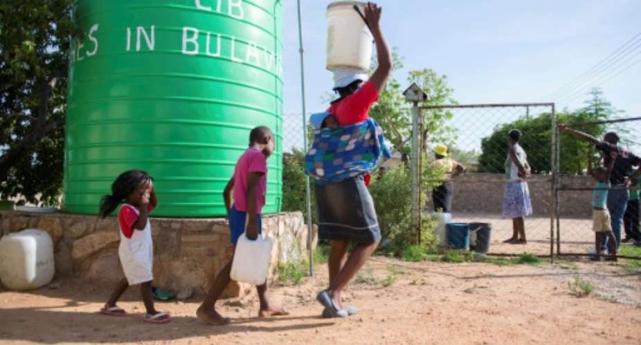 A woman and her children carry water buckets fetched from a tank installed at a church at Luveve on the outskirts of Bulawayo, Zimbabwe on November 24, 2016.  By ZINYANGE AUNTONY AFPFile