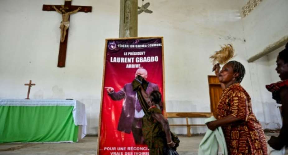 A woman dusts a poster reading 'President Laurent Gbagbo arrives for a true reconciliation of Ivorians' before a mass in his hometown of Mama.  By SIA KAMBOU AFP