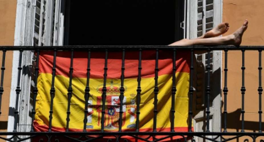 A woman sunbathes behind a Spanish flag on her balcony in Madrid during the national lockdown.  By Gabriel BOUYS AFP
