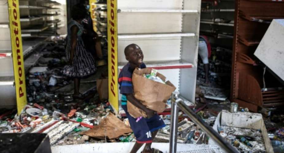 A young boy collects food and drinks from a burnt down and looted Auchan supermarket in an upscale Dakar neighbourhood.  By JOHN WESSELS AFP