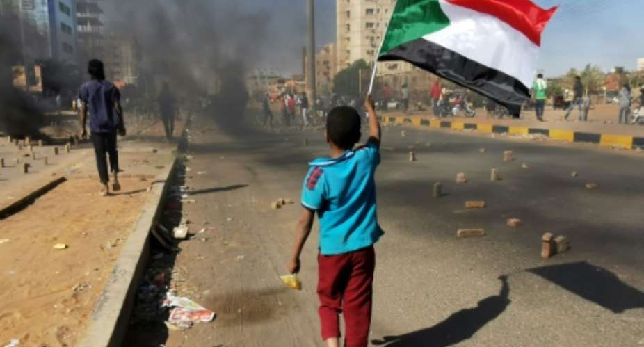 A young boy waves a Sudanese national flag as protesters block a street in the capital Khartoum, during a demonstration against the killing of dozens in a crackdown since last year's military coup, on January 20, 2022.  By ASHRAF SHAZLY AFP
