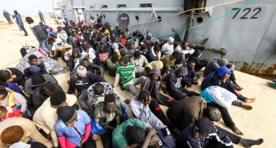 African migrants rescued from a ship off the coast of Zawiyah, west of the Libyan capital Tripoli, sit at the dock at the capital's naval base on March 10, 2018.  By MAHMUD TURKIA AFP
