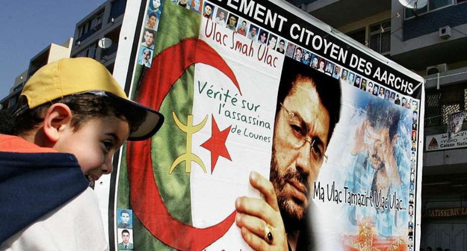 An Algerian boy(L) smiles in front of a placard with the picture of murdered singer Matoub Lounes.  By Fayez Nureldine (AFP/File)