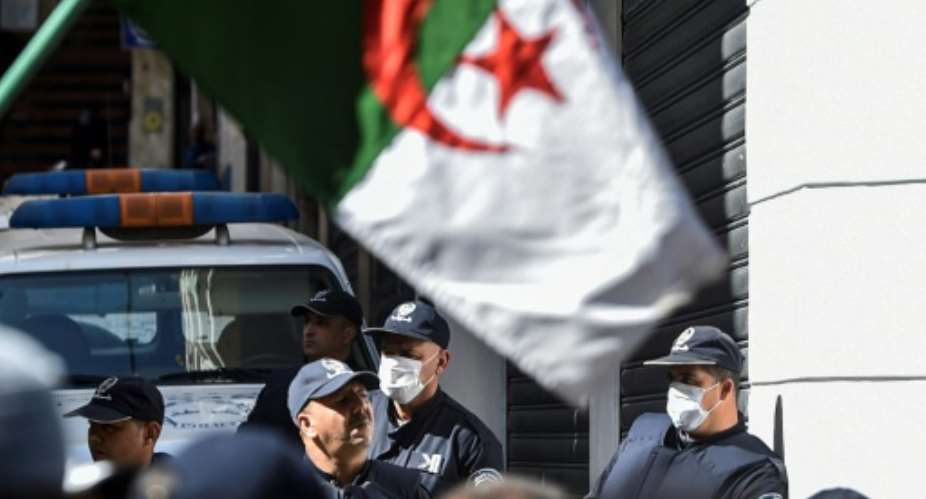 Algerian police wearing face masks stand as protesters march past during an anti-government demonstration in the capital Algiers on March 6.  By RYAD KRAMDI AFPFile