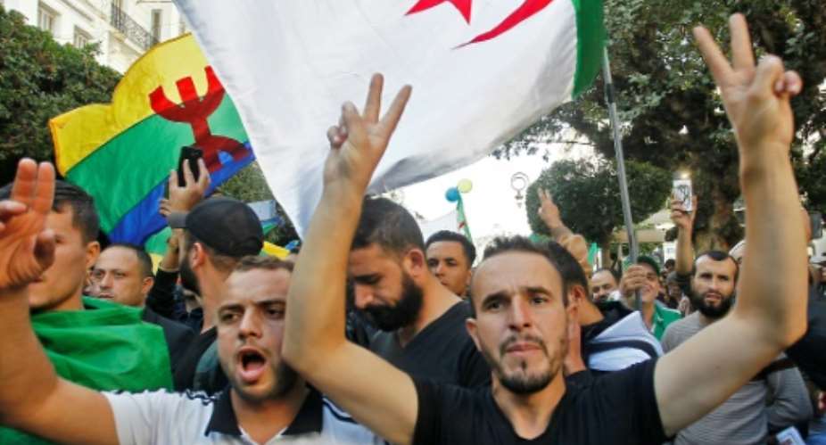 Algerian protesters, with the Berber flag in the background, chant slogans during anti-government demonstrations in the capital Algiers.  By - AFP