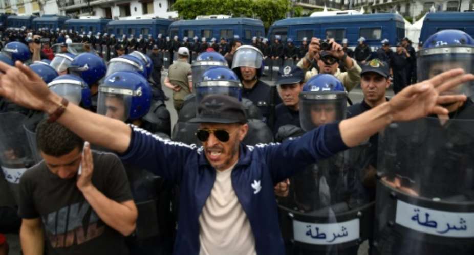 Algerian security forces stand guard behind protesters in the capital Algiers on Friday.  By RYAD KRAMDI AFP