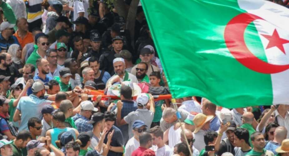 Algerians carry a protester on a stretcher at a weekly demonstration on July 5, 2019.Algerian police have opened an investigation after a video circulated online appeared to show protesters being beaten by security forces.  By - AFP
