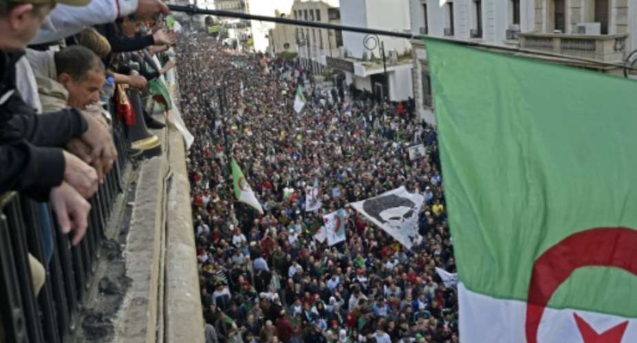 Algerians wave a national flag from a balcony as they watch anti-government demonstrators march in the capital Algiers on Friday.  By RYAD KRAMDI AFP