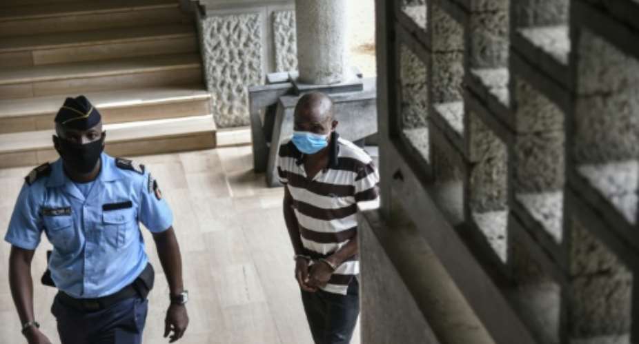 Amad Oueremi tee-shirt ray, ancien chef de guerre et milicien accus d'assassinats massifs dans l'Ouest de la Cte d'Ivoire en 2011, arrive  son procs  Abidjan, sous escorte policire, le 1er avil 2021..  By SIA KAMBOU AFP