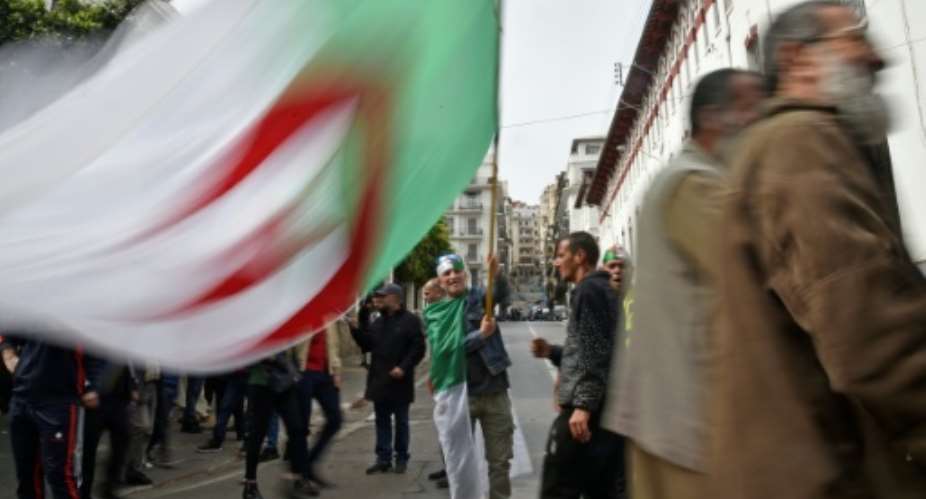 An Algerian protester waves the national flag during a weekly anti-government demonstration in the capital Algiers on March 13 before the rallies were suspended because of the novel coronavirus.  By RYAD KRAMDI AFP