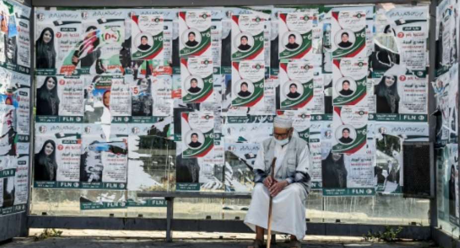 An Algerian sits in front of campaign posters in the capital Algiers on Friday, a day before legislative elections.  By RYAD KRAMDI AFP