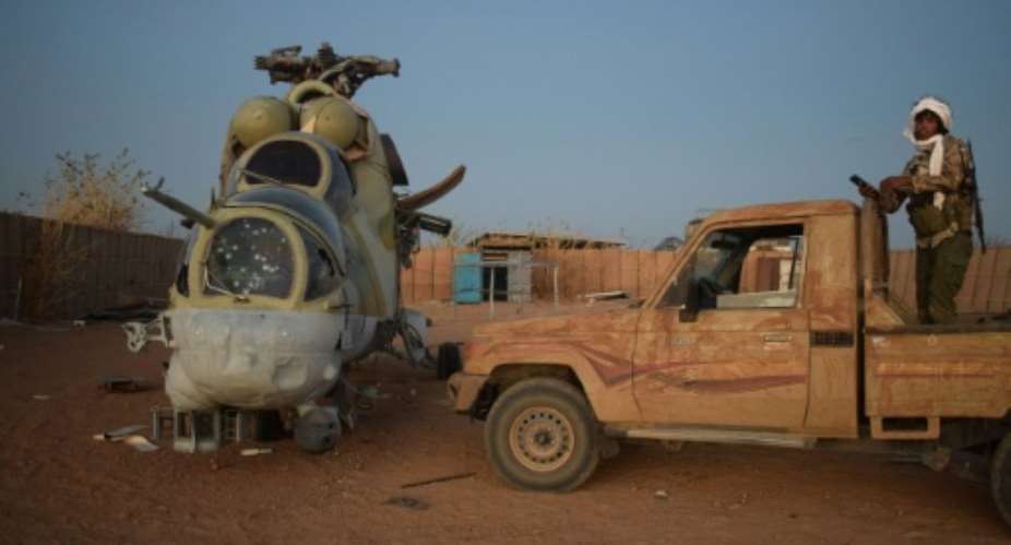 An Azawad Liberation Front fighter next to a damaged Mi-24 helicopter at the former Russian mercenary barracks in Kidal on May 6.  By - (AFP)