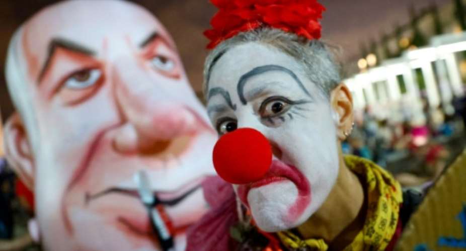 An Israeli woman in a clown outfit mocks a giant head costume representing Prime Minister Benjamin Netanyahu as she takes part in a demonstration in Tel Aviv against the government and an imminent and unprecedented second nationwide virus lockdown.  By JACK GUEZ AFP