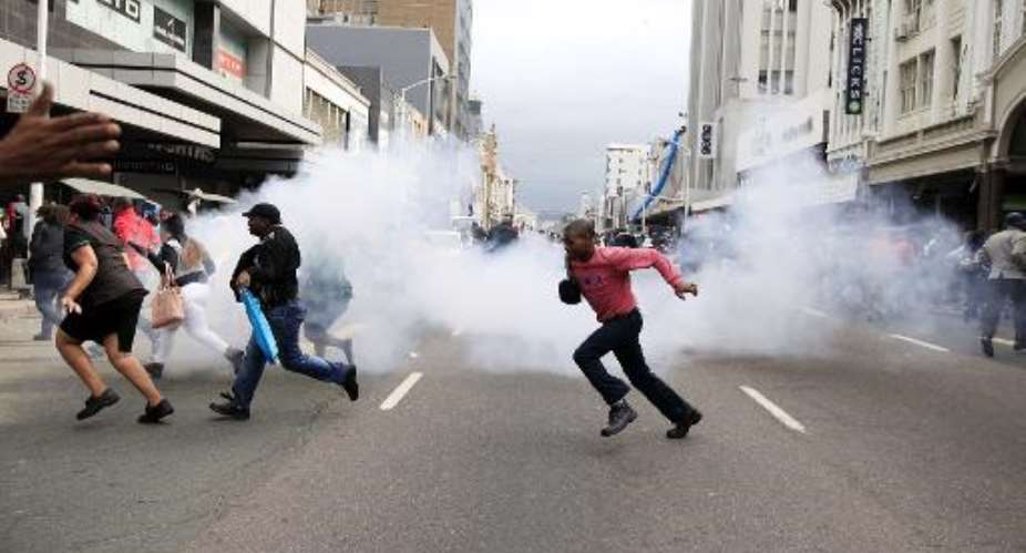 People run for cover from a stun grenade and tear gas after a skirmish between locals and foreign nationals as thousands of people take part in the peace march against xenophobia in Durban, South Africa, on April 16, 2015.  By  AFP