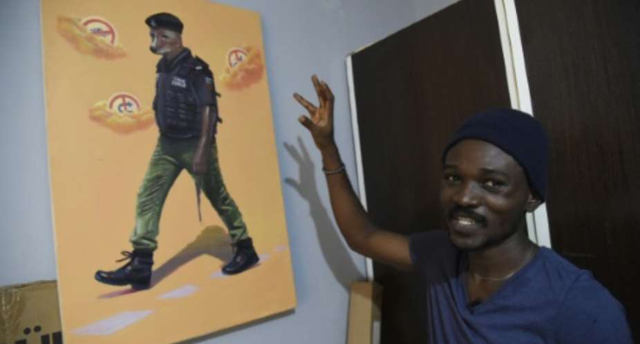 Artist Julius Agbaje shows a painting of a police officer with dog's head, entitled 'Mad Dog'.  By PIUS UTOMI EKPEI AFP