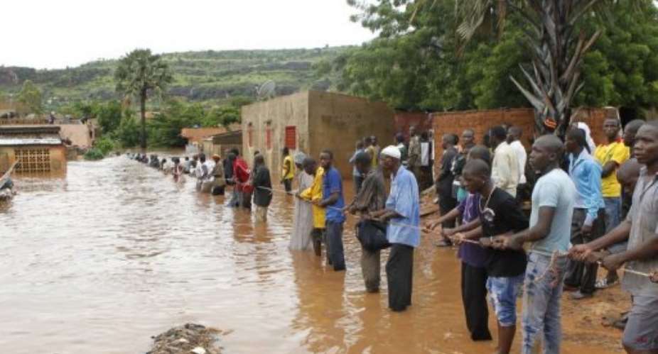People hold a rope to help rescuers climbing down a roof of a house in a flooded area of Bamako, on August 28, 2013.  By Habibou Kouyate (AFP/File)