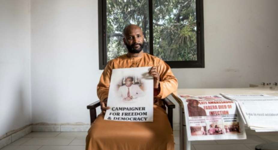 Baba Hydara holds a poster of his late father Deyda Hydara who was gunned down in 2004.  By MUHAMADOU BITTAYE AFP