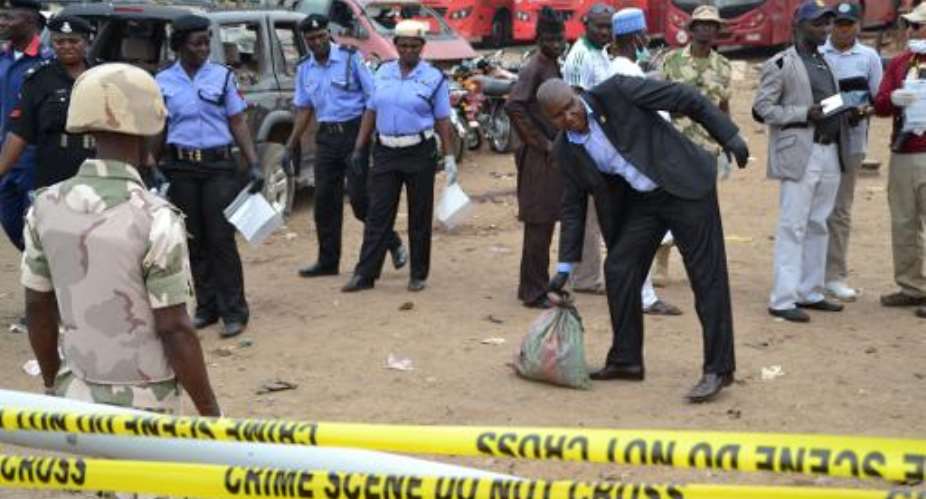 Security forces stand guard as an investigator carries a bag of items recovered from the site of a bomb blast in Abuja on April 15, 2014.  By  AFPFile