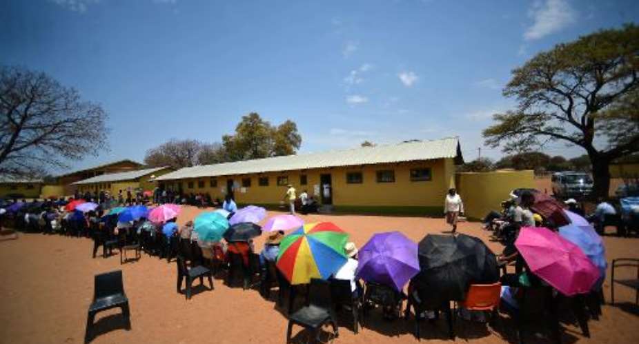 Voters sit under umbrellas as they queue outside a polling station in the capital Gaborone to cast their ballot during the general elections in Botswana, on October, 24 2014.  By Monirul Bhuiyan AFP