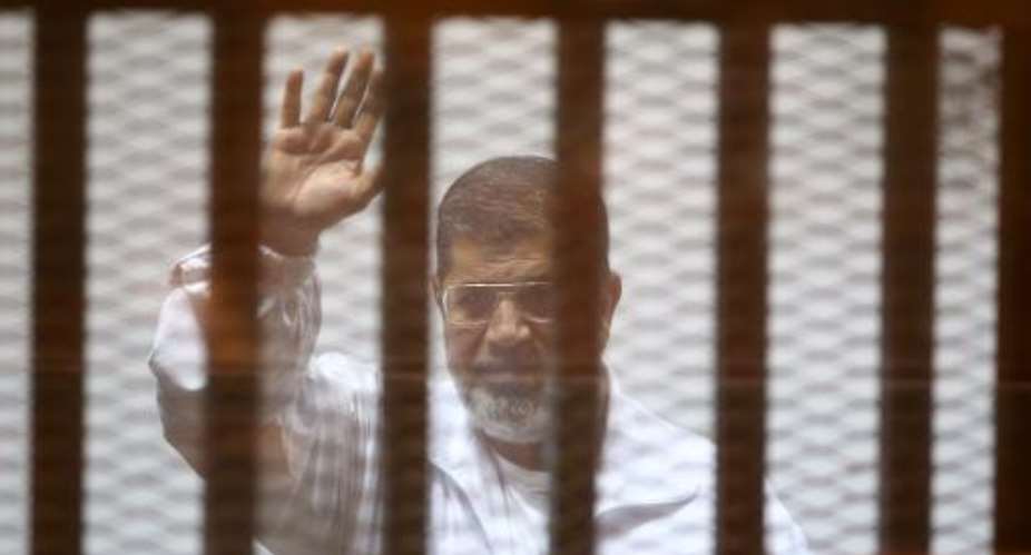 Egypt's deposed Islamist president Mohamed Morsi waves inside the defendants cage during a trial in Cairo on December 7, 2014.  By Ahmed Ramadan AFPFile
